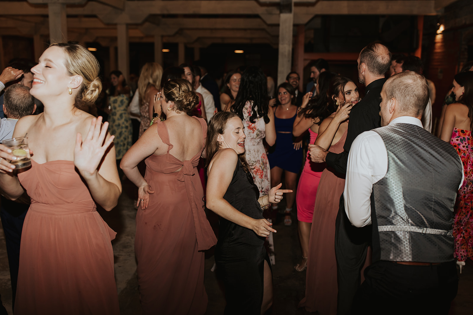 Guests of all ages fill the dance floor at a wedding reception, enjoying energetic DJ entertainment and dancing in formal attire under warm ambient lighting, creating a lively and memorable celebration atmosphere.
