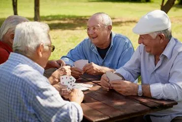 four-seniors-playing-cards-outdoor-picnic-table.webp