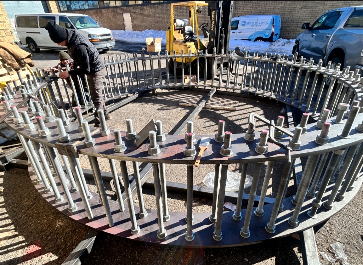 Workers assembling a large circular steel anchor bolt template