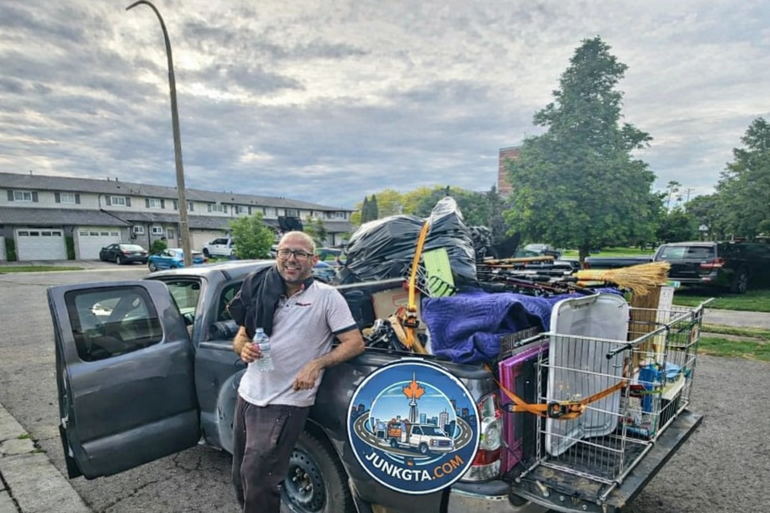 What Can I Put in a Construction Debris Removal Bin? A Junk GTA crew member stands beside a pickup truck loaded with various junk items, such as large bags and miscellaneous furniture.