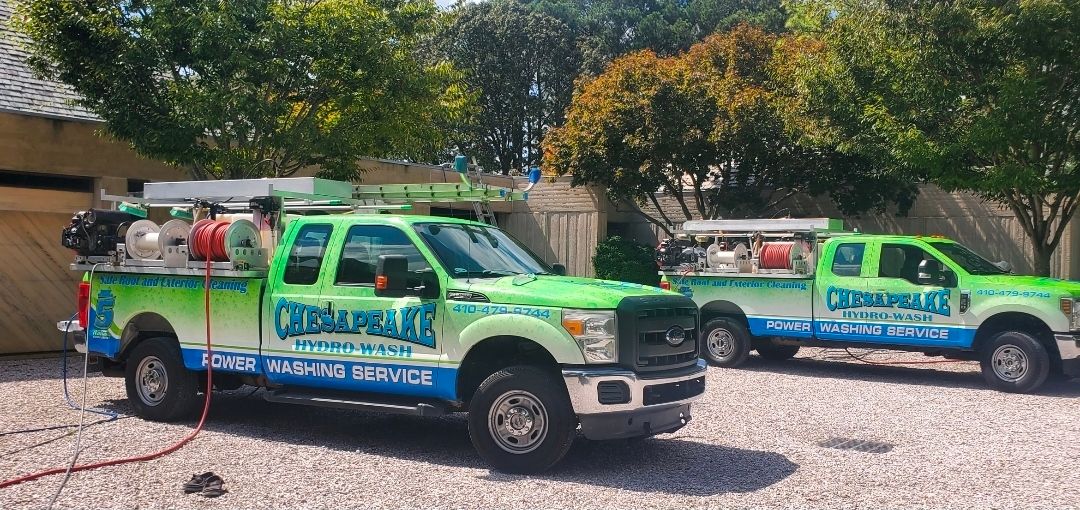 Two Chesapeake Hydro-Wash service trucks equipped for power washing and soft washing are parked on a residential driveway