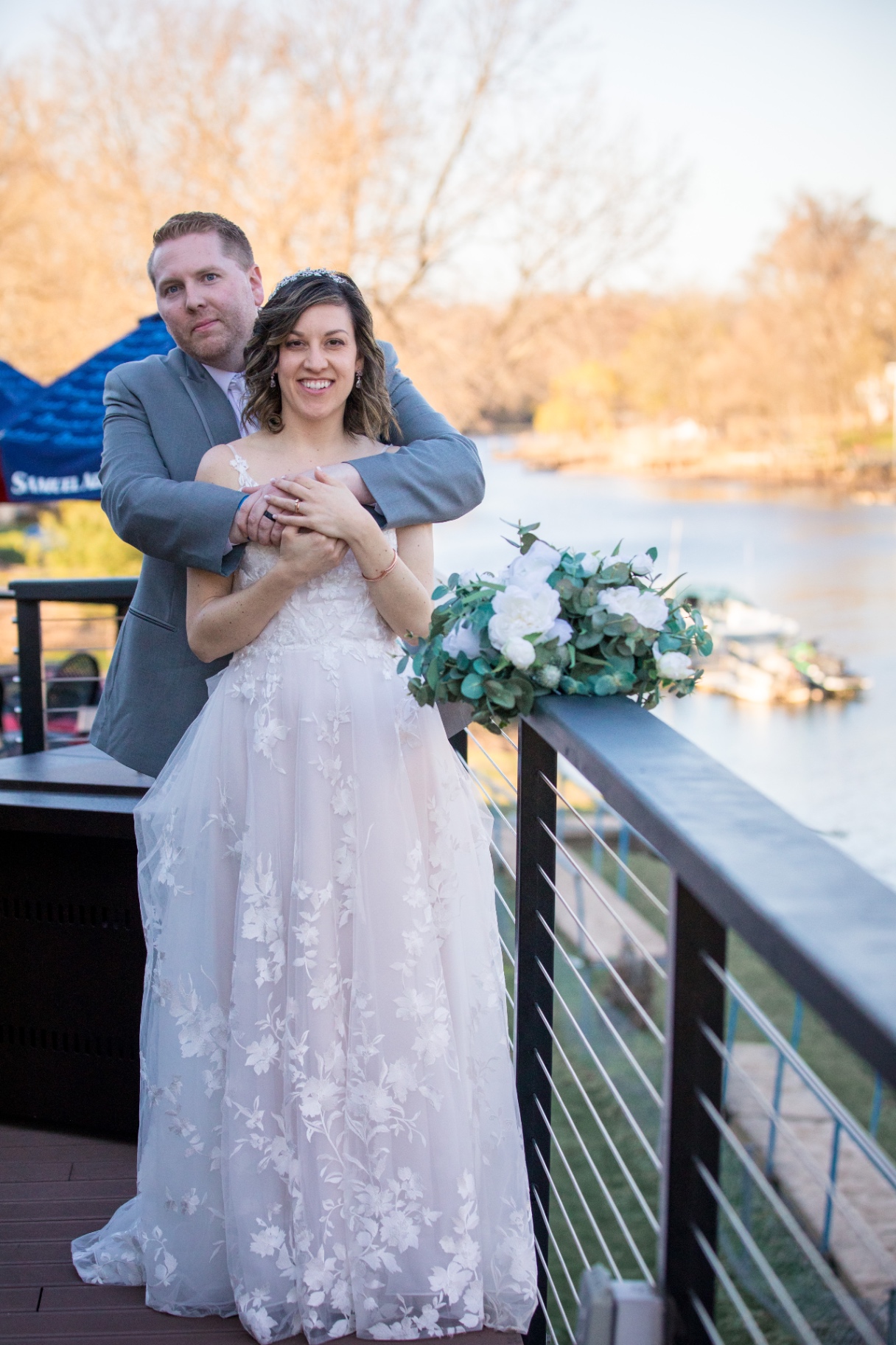Bride and groom share a romantic embrace and kiss on an outdoor deck overlooking the river