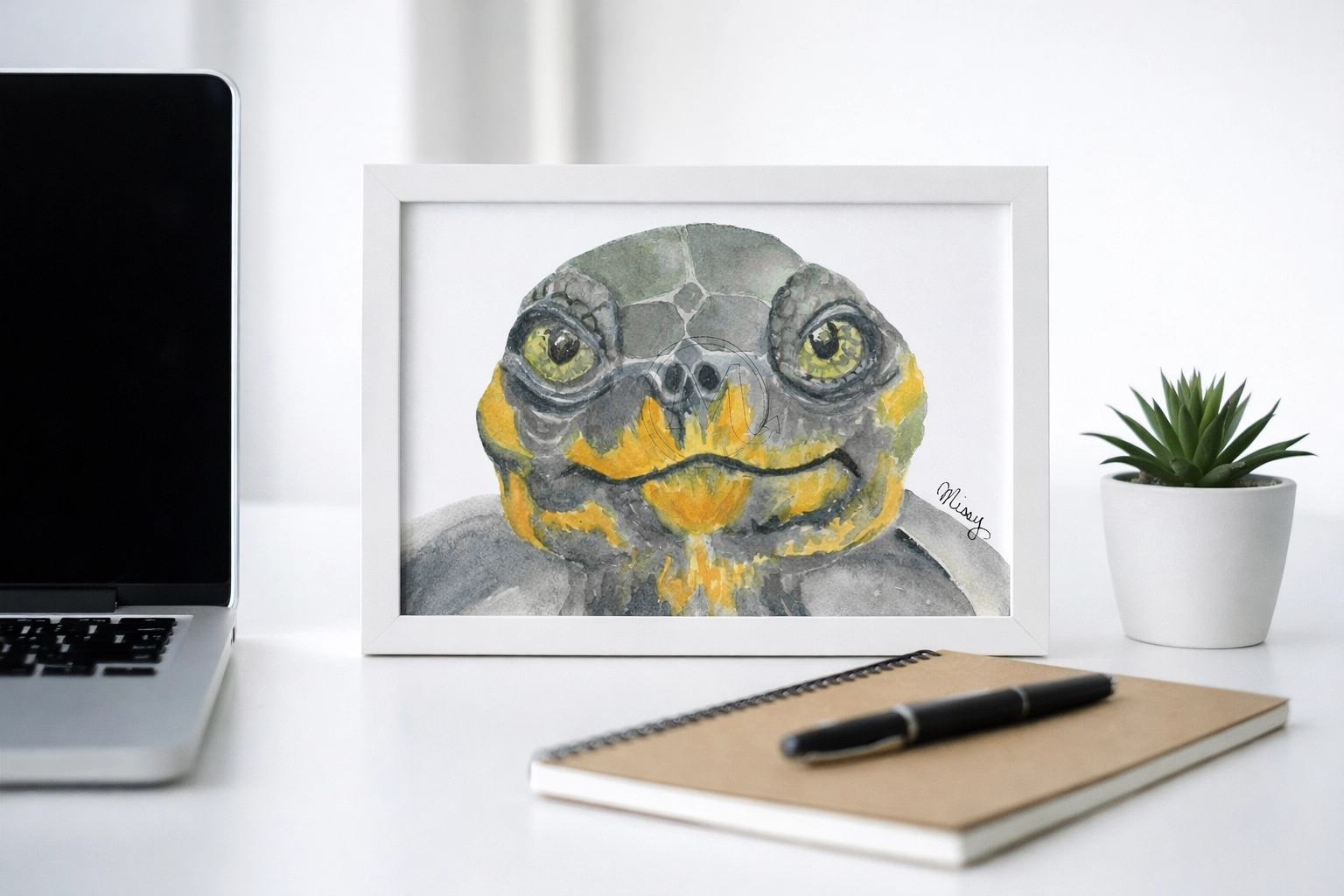 Lifestyle mockup of Missy’s signed turtle watercolor print framed in a desktop setup