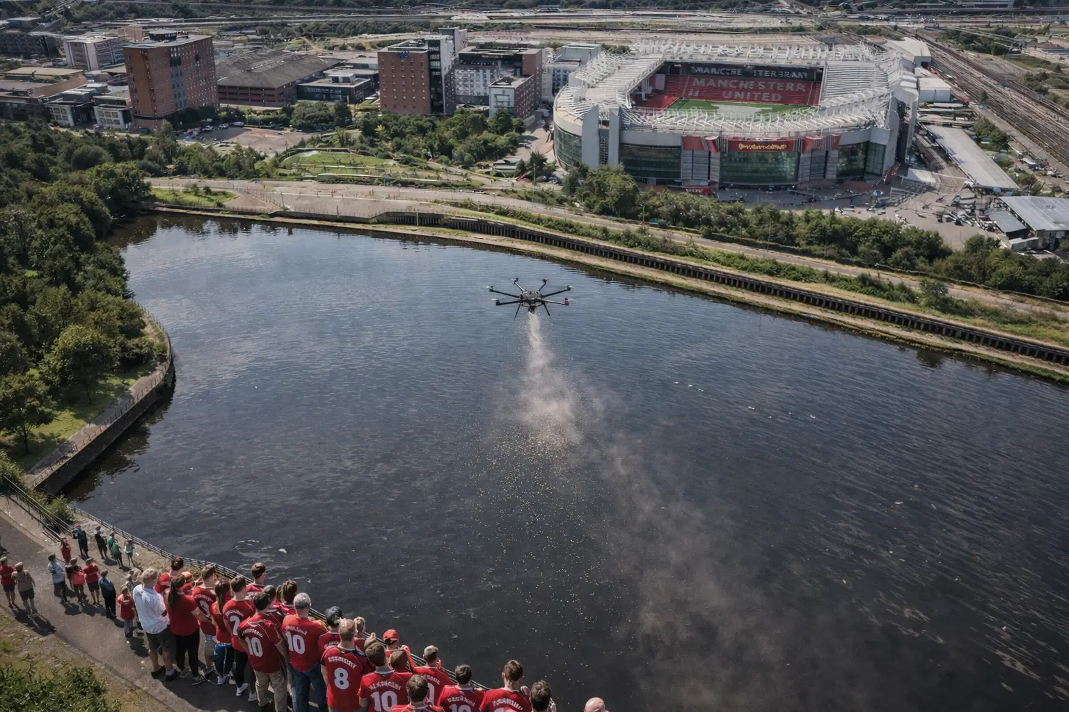 A large group wearing red football shirts gathers by the waterside. A drone, operated by Aerial Ashes Matt, gracefully scatters ashes over the water, providing a dignified tribute for a loved one.