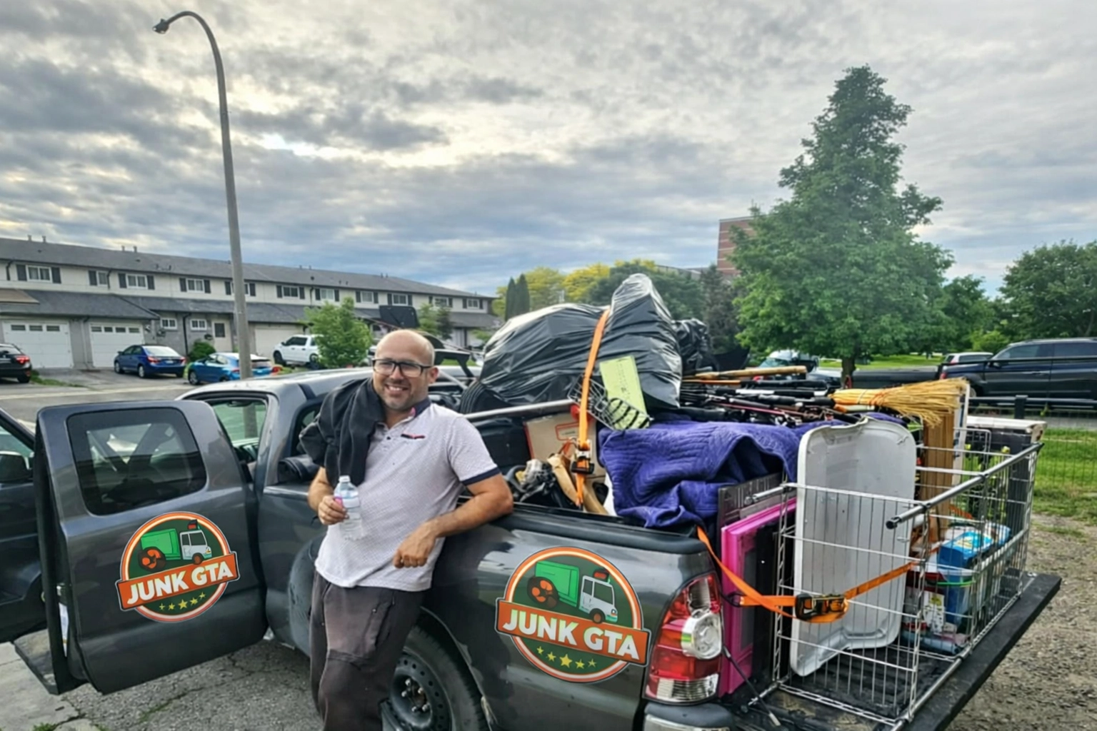Professional Junk Removal vs DIY Innisfil: The Final Verdict Roman, owner of Junk GTA, standing by his 2014 Toyota Tacoma loaded with junk for removal in a residential neighborhood.