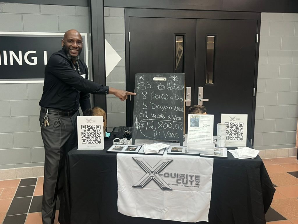 Lakota East Career Fair - Earning Potential Chalkboard Rodriguis Hampton pointing to the $72,800 annual earning potential breakdown at Lakota East Career Fair.