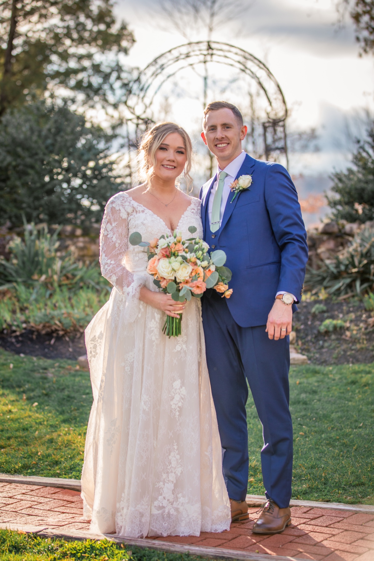 Bride and groom pose together outdoors after their ceremony, framed by a garden arch