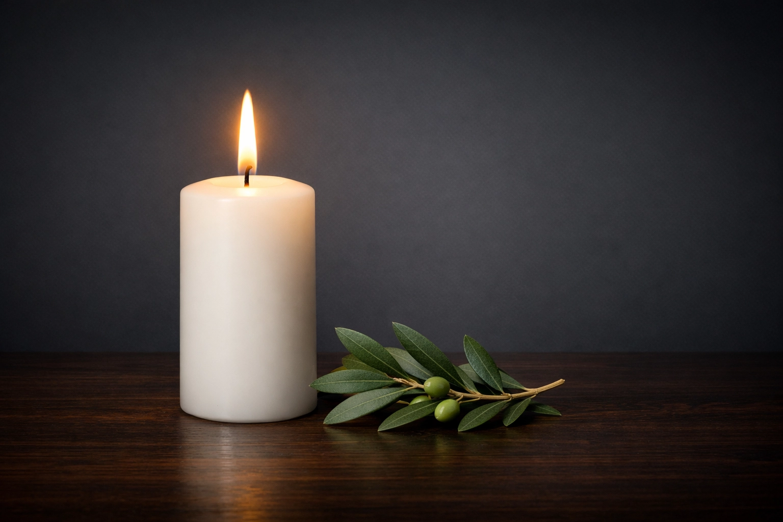A burning white candle and olive branch on wood, symbolizing prayer, reflection, and a hopeful future for justice.