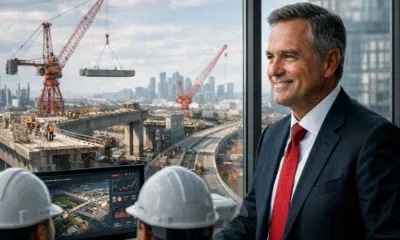 A business executive in a suit stands in a modern high-rise office, observing engineers in hard hats monitoring data on screens. Large windows reveal a major Canadian infrastructure project with cranes and partially built bridges, set against a city skyline.