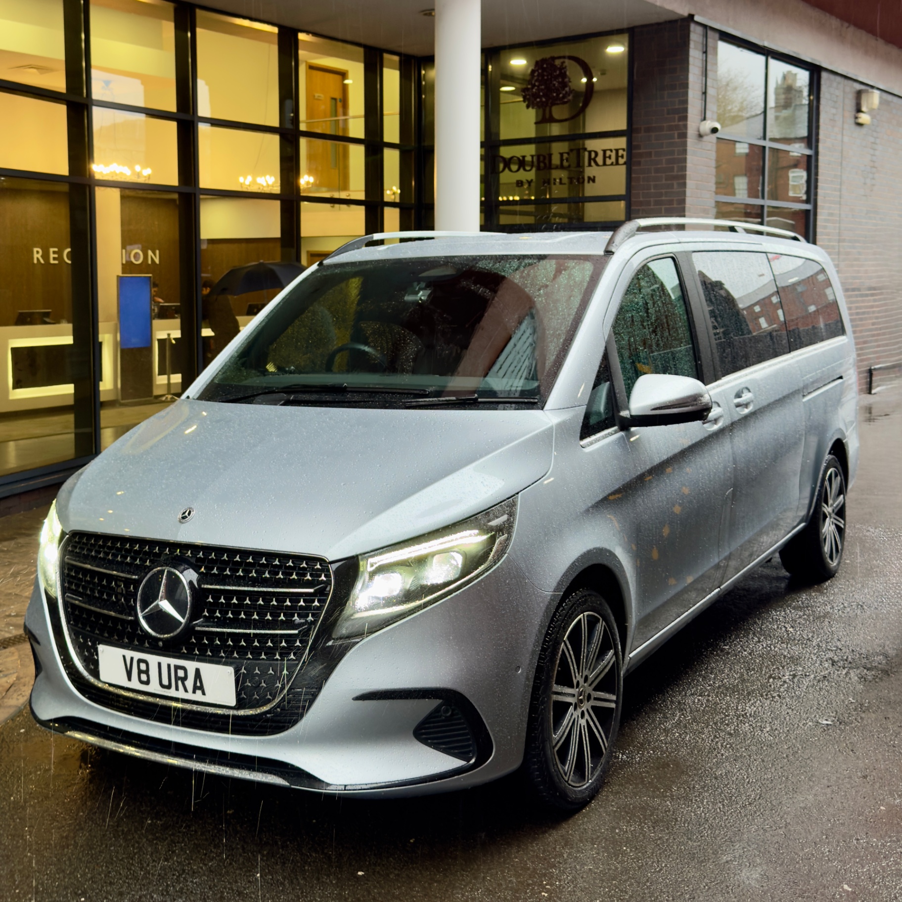 A silver Mercedes-Benz luxury chauffeur vehicle from Aura Journeys is parked outside the DoubleTree by Hilton hotel