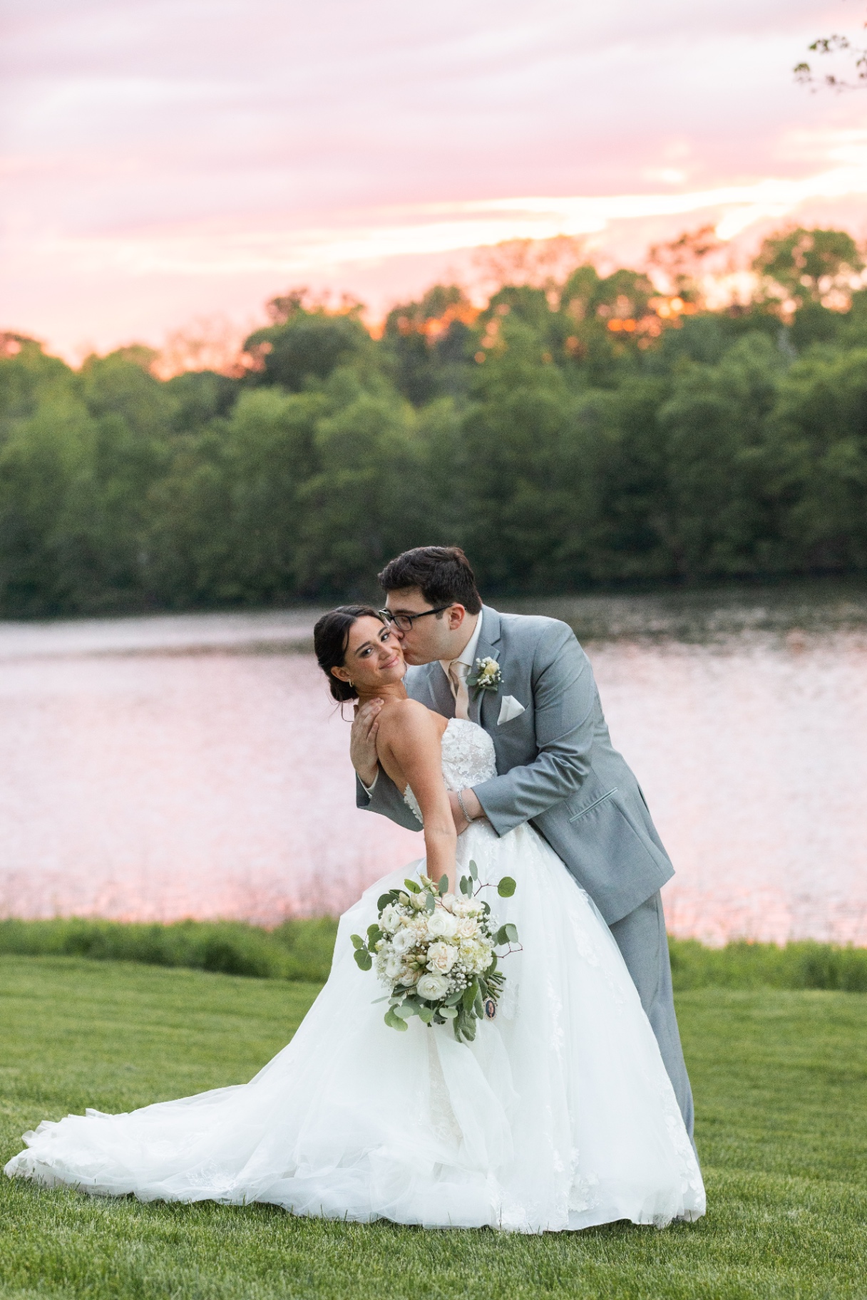Bride and groom beside lake at sunset