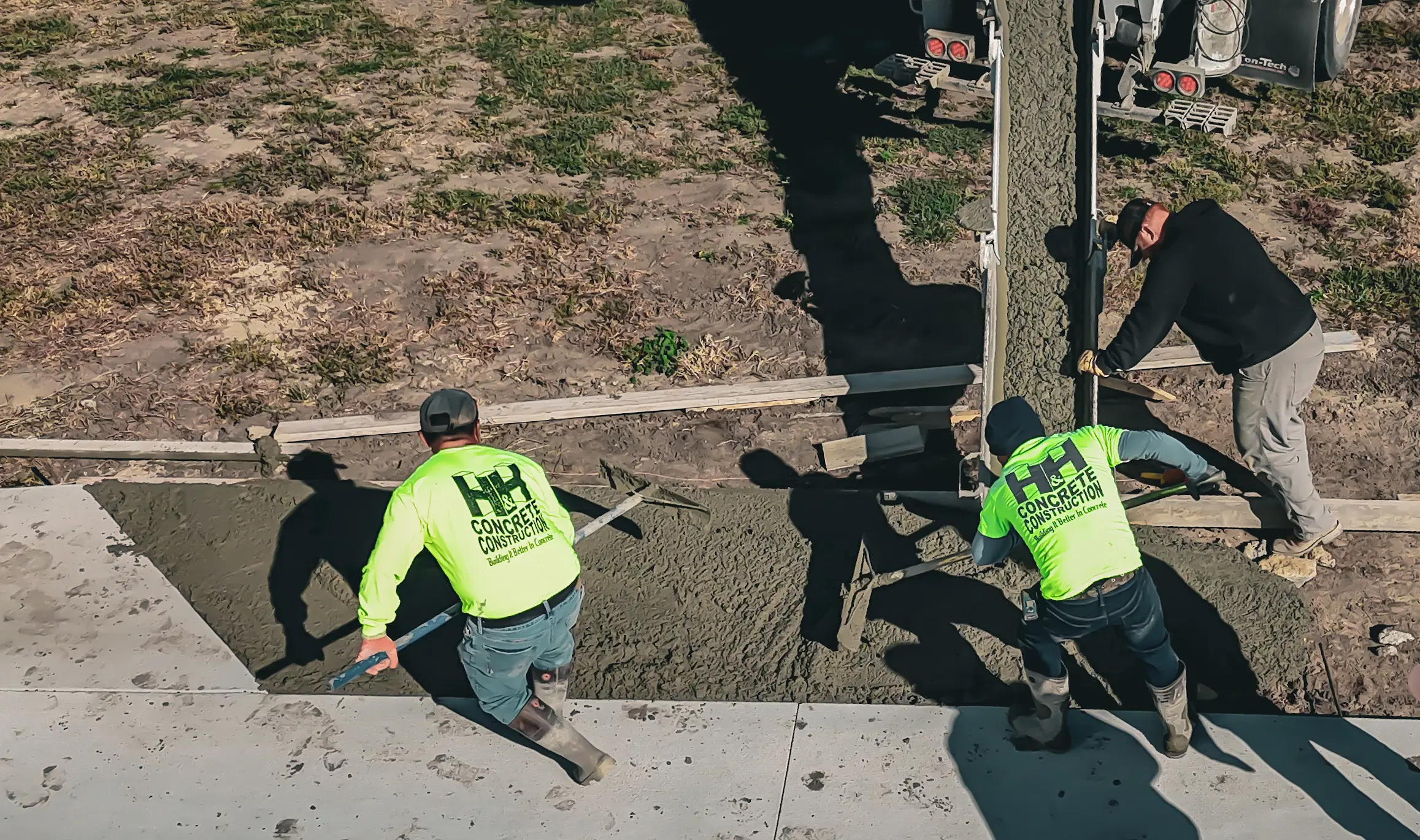 H&H Concrete and Construction crew pouring and leveling fresh concrete for a new sidewalk, using professional tools.