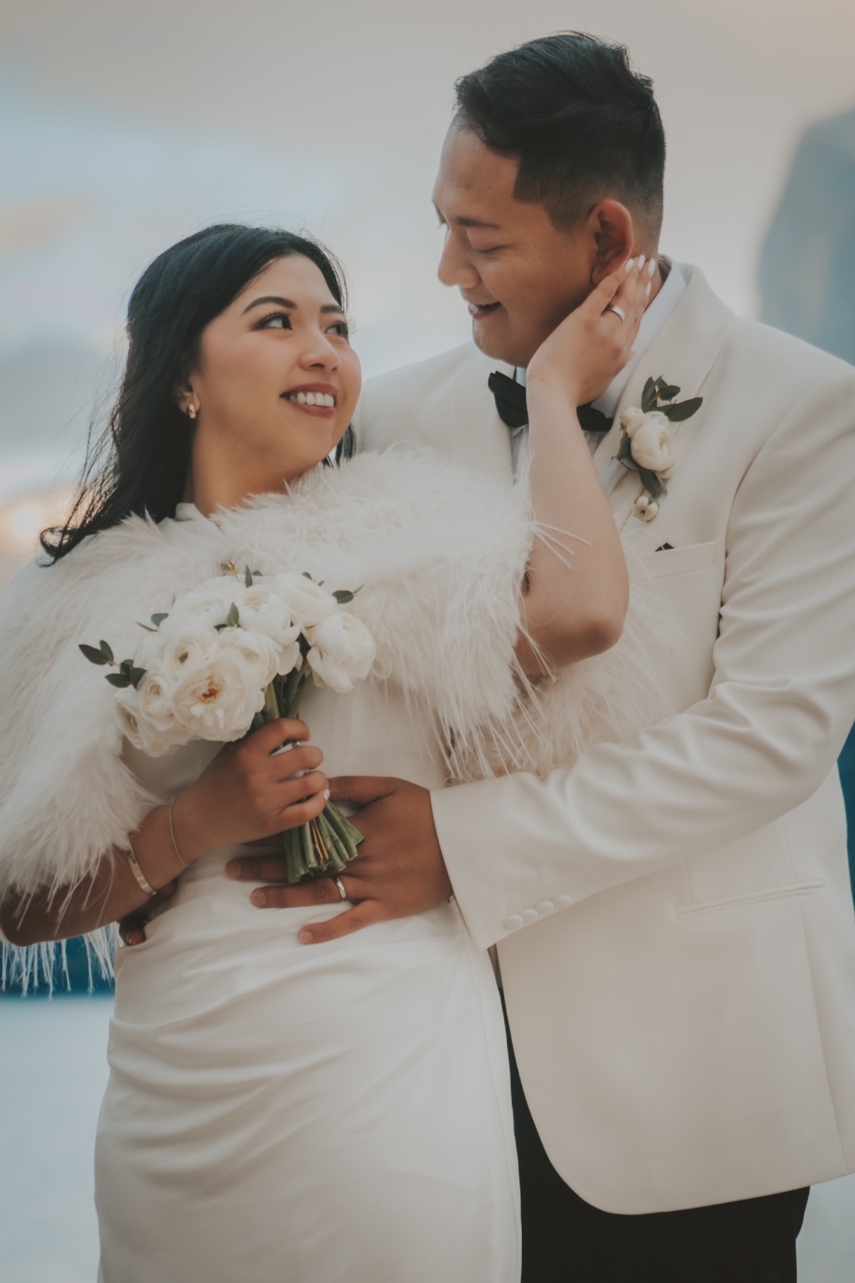 A newlywed couple in elegant wedding attire holding a white bouquet
