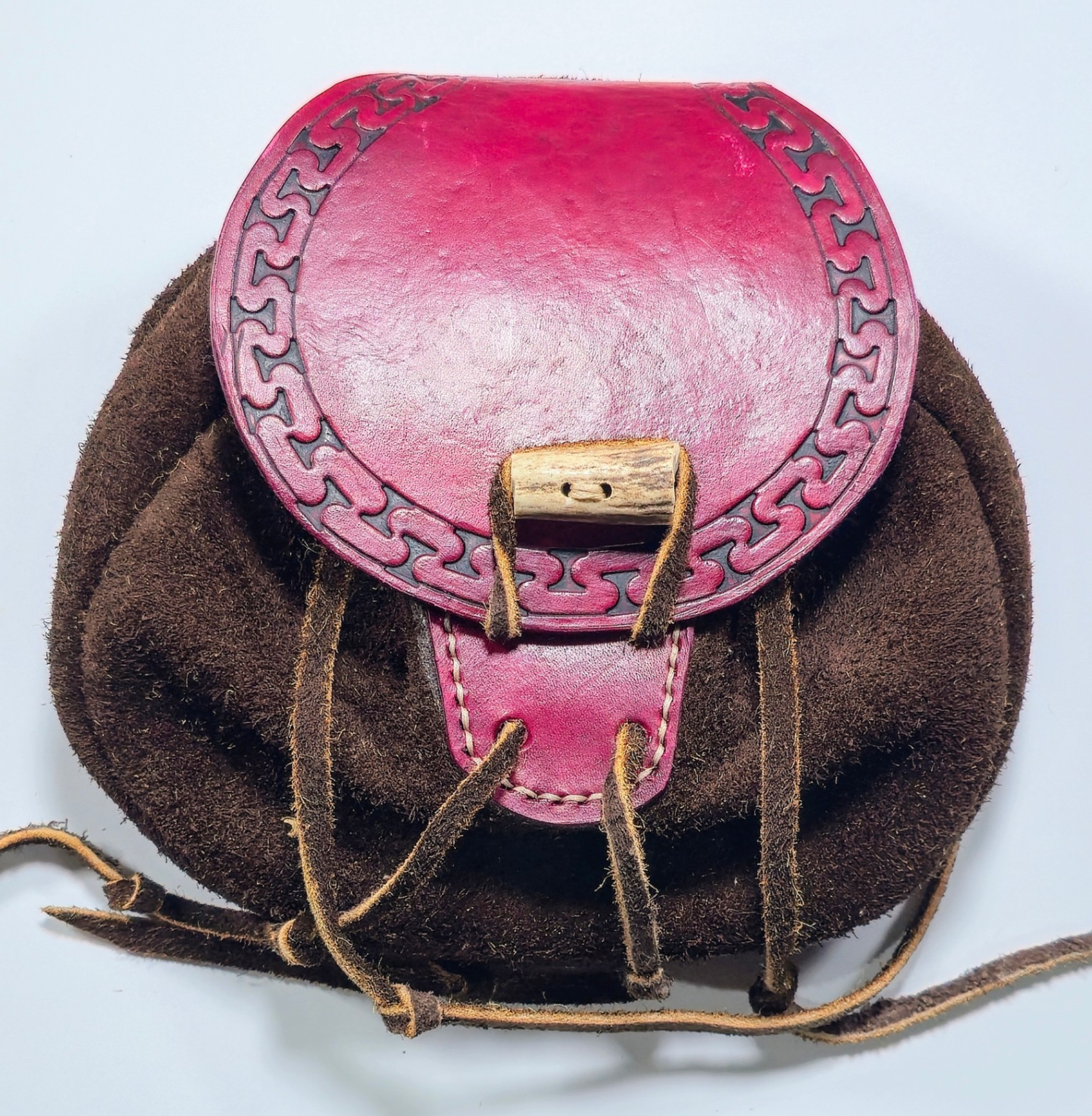 Handcrafted leather pouch with reddish-pink tooled flap and toggle closure.
