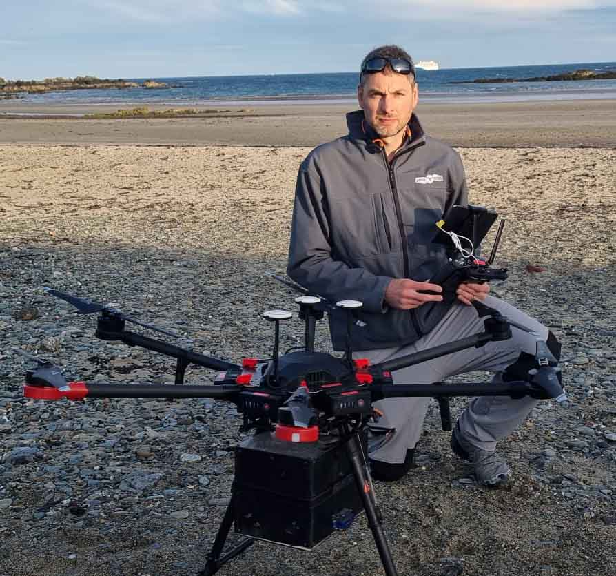 A licensed drone operator in branded outdoor gear prepares a specialised drone