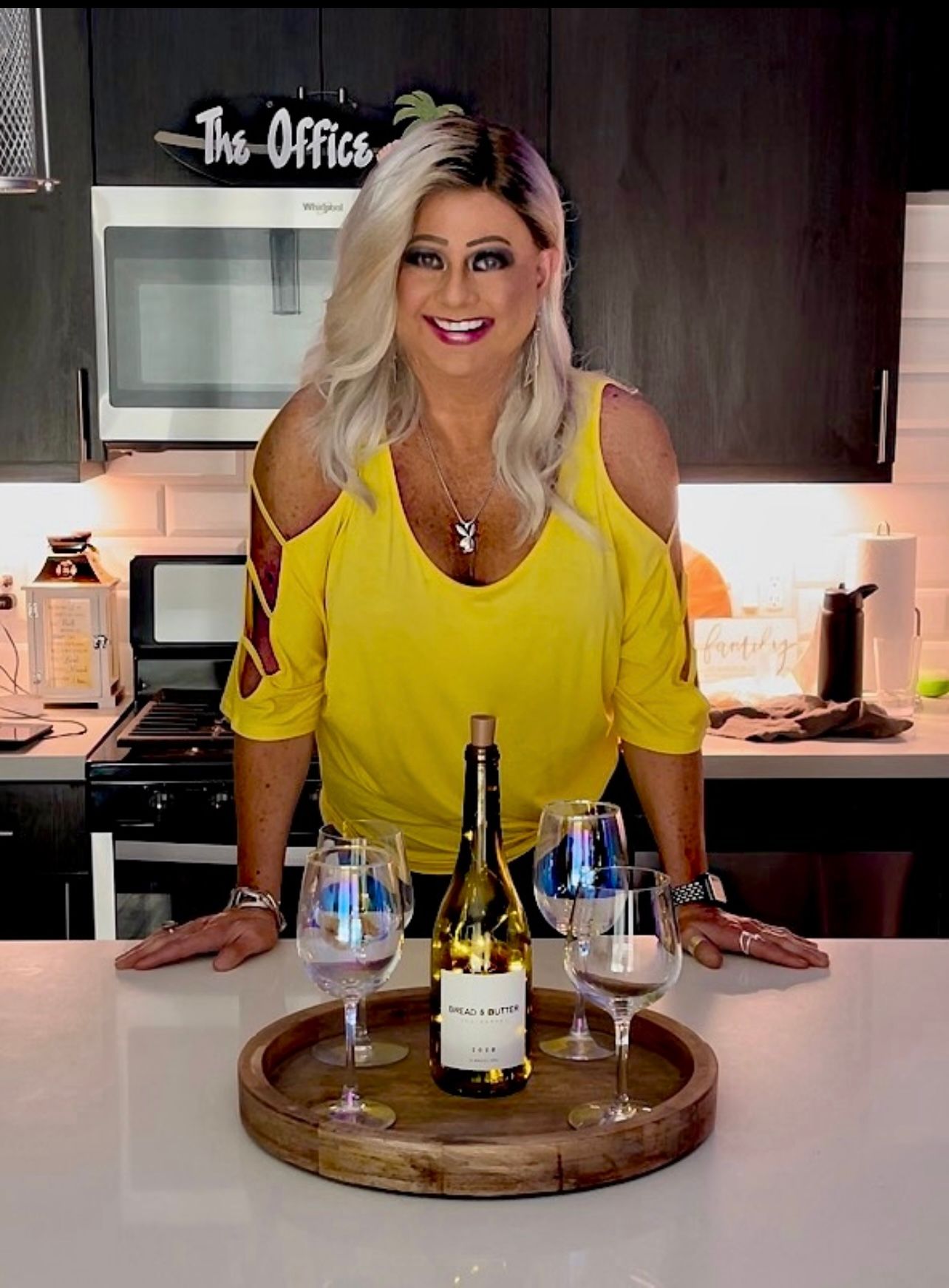 Maddie 33 Maddie in a bright yellow, cold-shoulder top in a modern kitchen with a bottle of Bread & Butter wine and wine glasses.