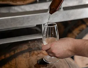 A hand carefully draws fresh spirit from a wooden barrel