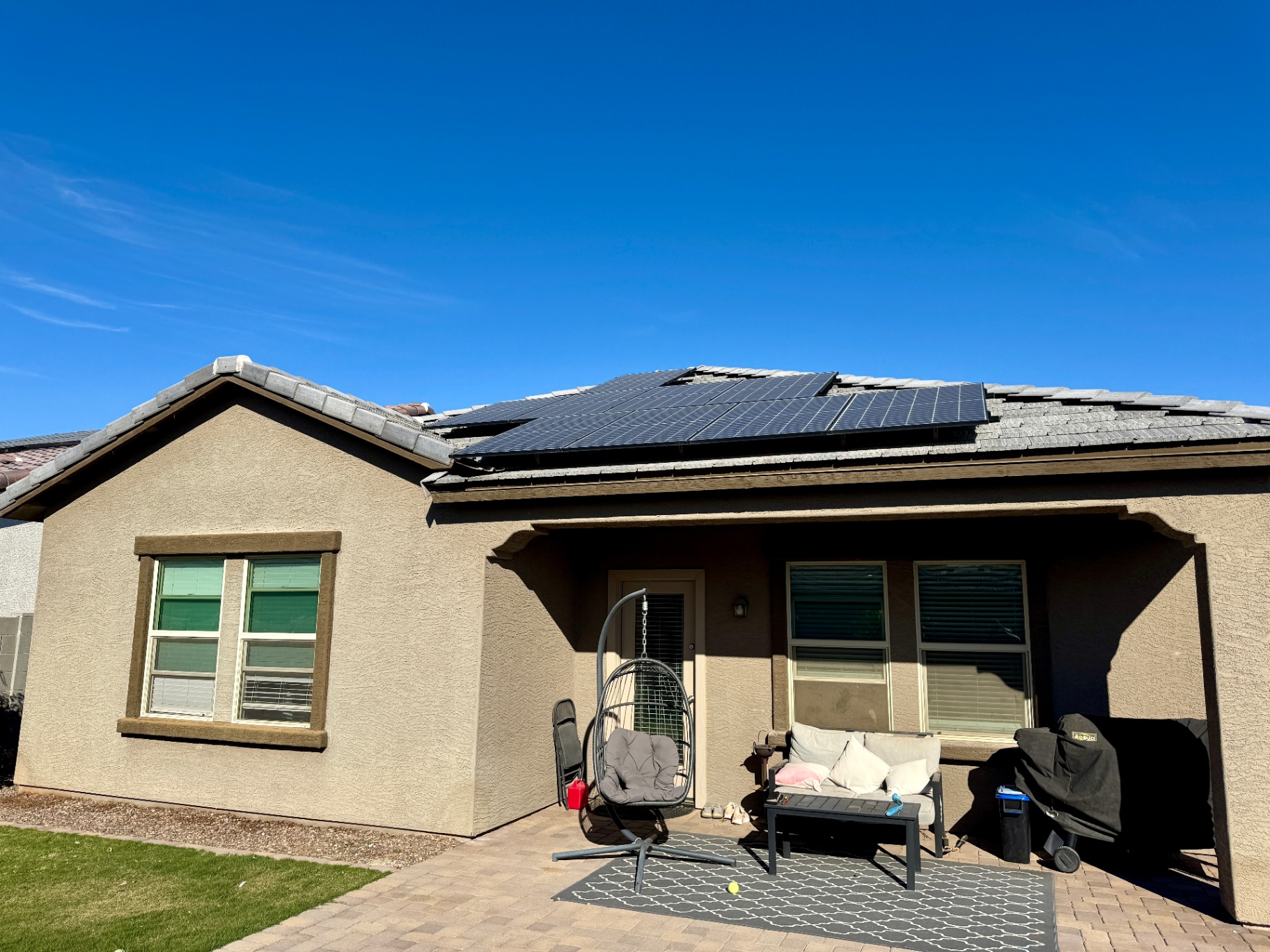 Single-story Arizona home with solar panels A single-story Arizona home featuring solar panels, a backyard patio, and simple landscaping. Includes a covered outdoor living area with seating, a hanging chair, BBQ grill, and paver patio, emphasizing energy efficiency and a relaxing backyard space ideal for everyday living or entertaining.