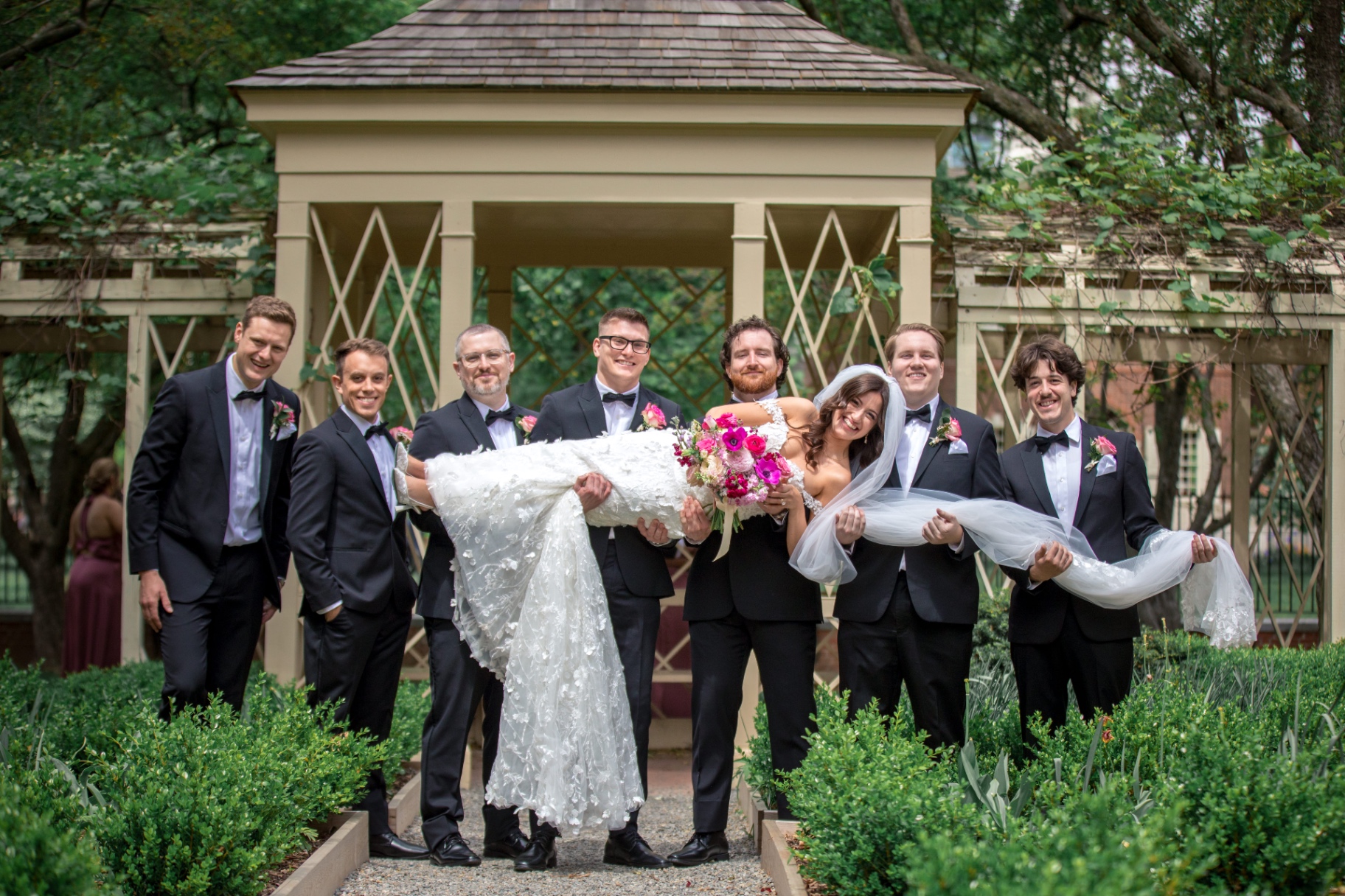 The groom and groomsmen joyfully lift the bride at the garden wedding