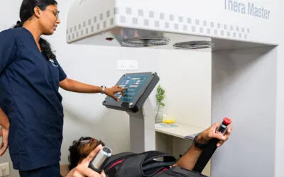 A Maana Health specialist operates the Thera Master device for non-surgical spinal decompression therapy. The patient is positioned comfortably on the treatment table, holding safety switches, while the therapist adjusts settings on the digital control panel.