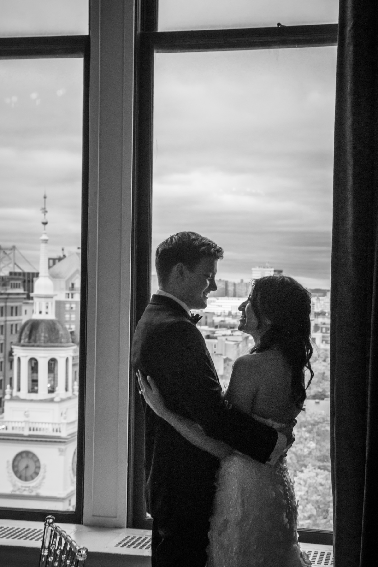 Bride and groom embrace in front of a large window