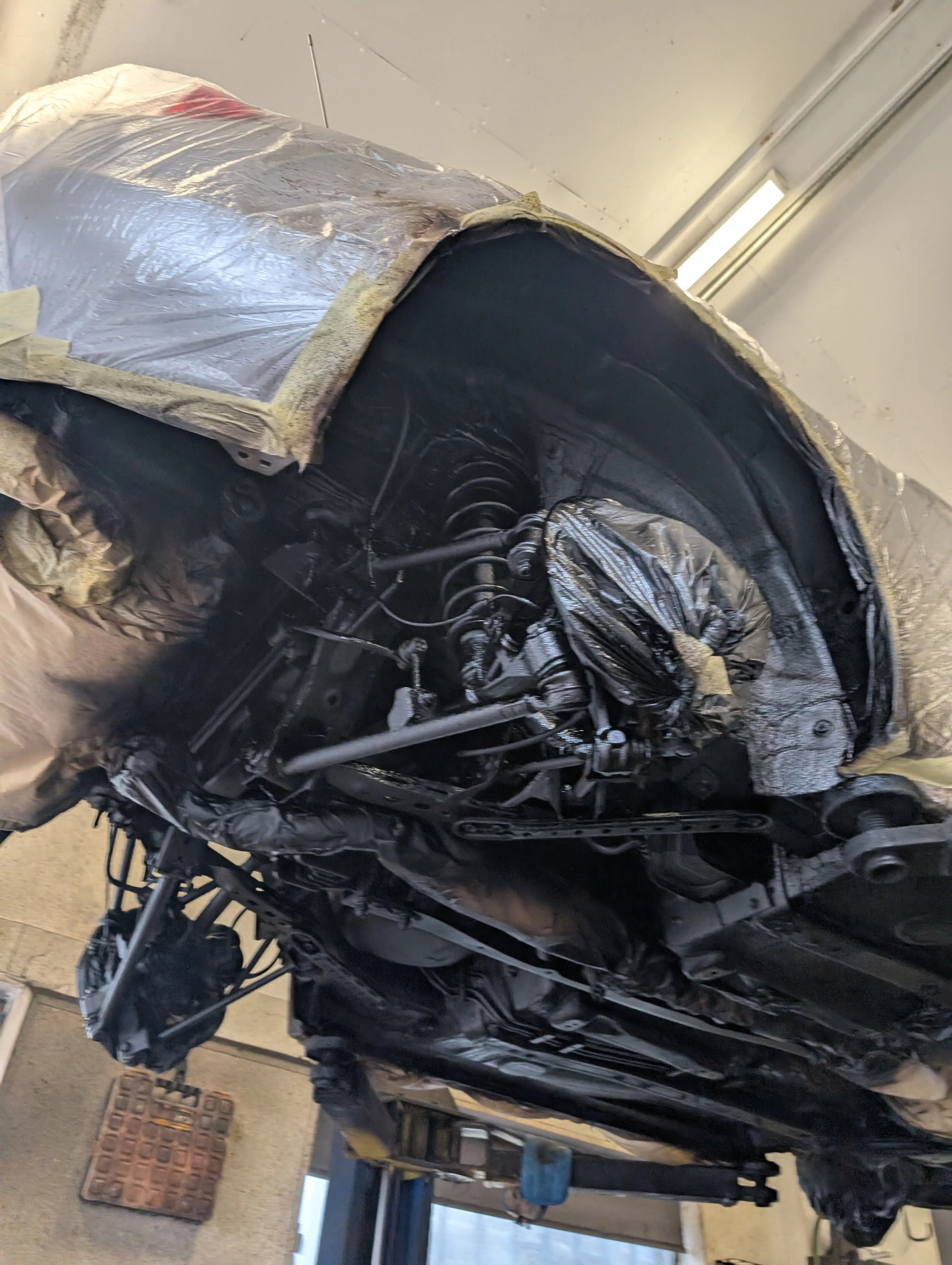 Vehicle on a hoist with the entire underbody masked in preparation for rust proofing treatment