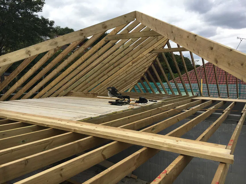 timber-roof-construction.webp Timber roof structure in progress, showing expertly aligned rafters and joists.
