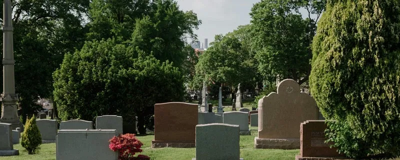 Well-maintained cemetery grounds with neat grass and headstones surrounded by mature trees.