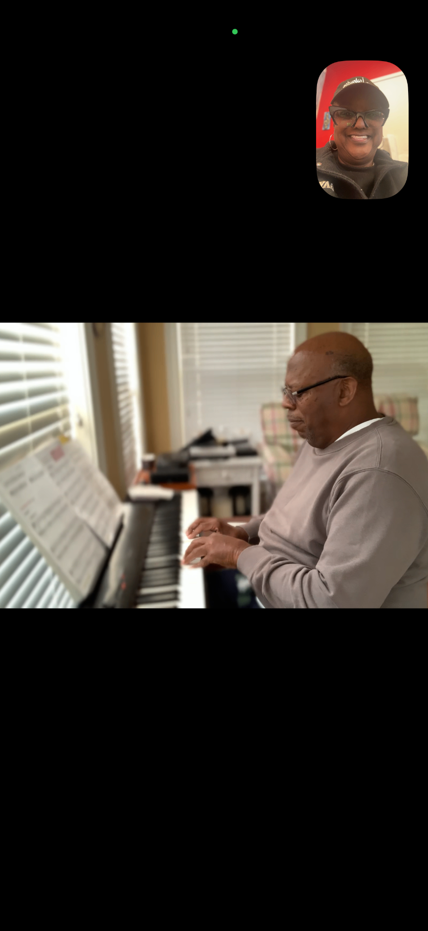 A student is seated at an electric piano, practicing with sheet music, during an online piano lesson