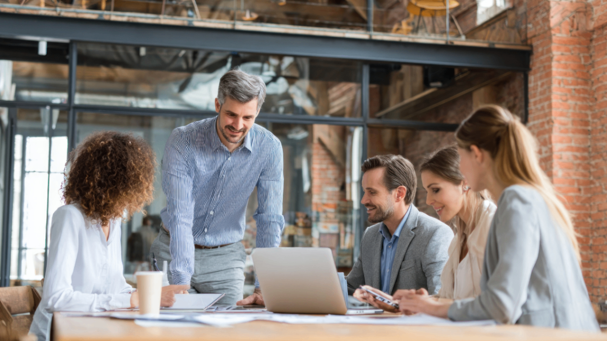 A diverse team of real estate professionals collaborates around a laptop in a modern office setting