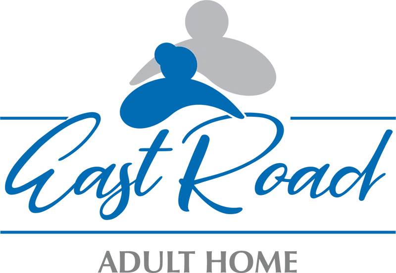 A senior resident in a wheelchair receiving individualized attention from a caregiver at East Road Adult Home.