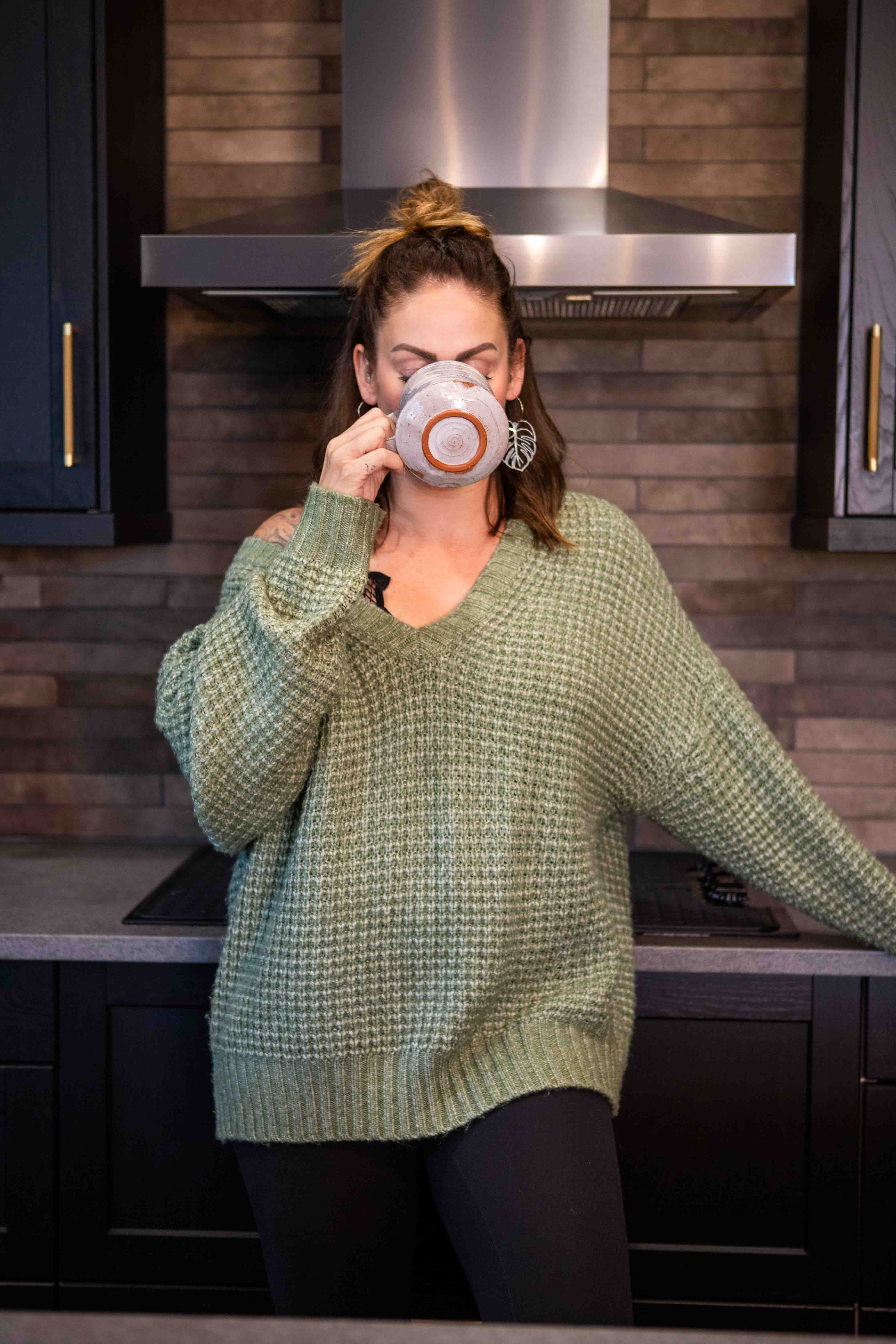 A midlife woman in a cozy green sweater enjoys a peaceful pause, illustrating the value of checking in with your energy.