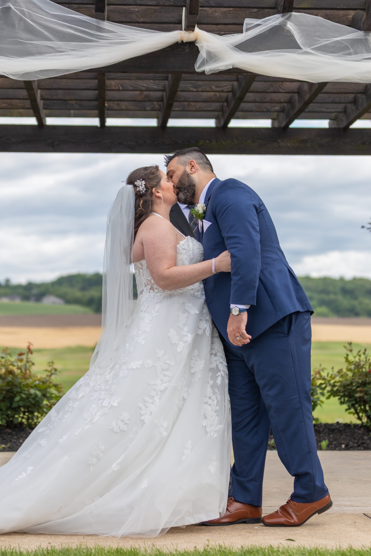 Natalie and Pat sharing a kiss beneath a vine-draped pergola at Olde Homestead