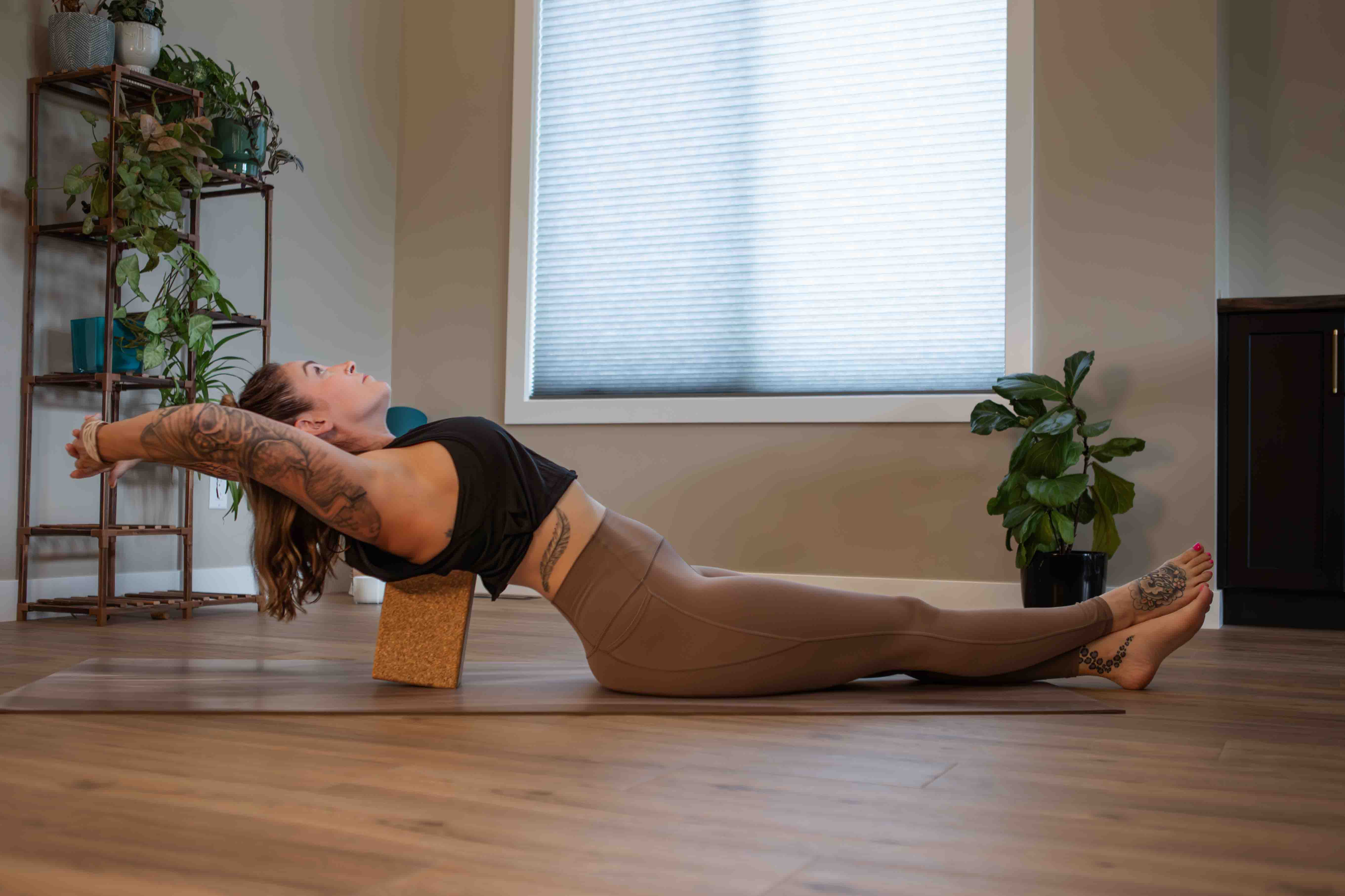 A woman practices a gentle supported backbend using a cork yoga block, a perfect restorative option for low-capacity days.