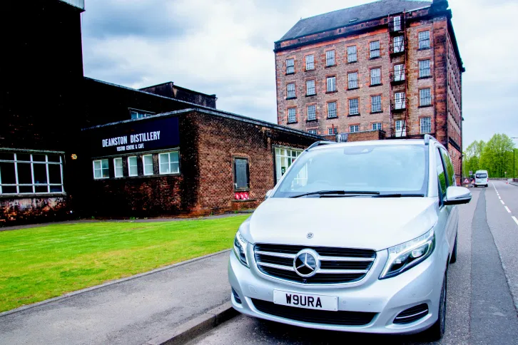 A luxury Aura Journeys vehicle parked outside the historic Deanston Distillery