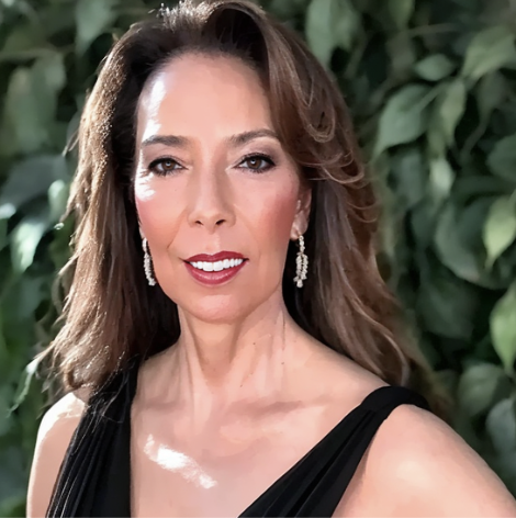 GG Sfreddo headshot, wearing sleeveless black top, gold earrings with a green floral backdrop