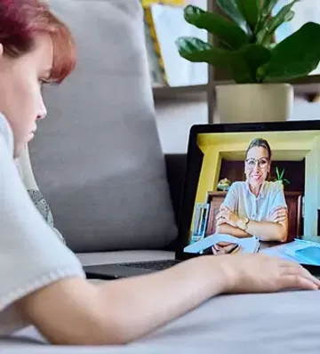 A young person participates in an online video session with a professional clinician from their comfortable living space.
