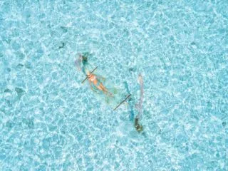 Aerial view of a person kayaking in a transparent kayak over clear turquoise waters.