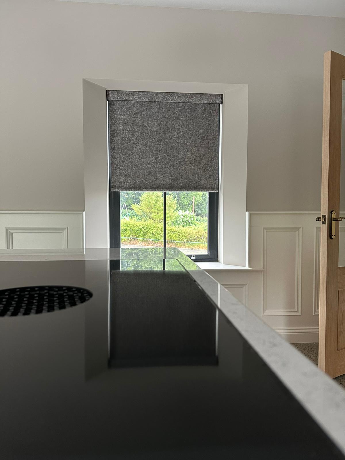 A modern kitchen window fitted with a bespoke grey roller blind, expertly measured and manufactured in-house by Fiesta Blinds.