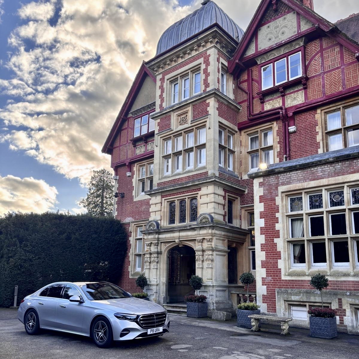 A silver Mercedes-Benz executive saloon from Aura Journeys outside an elegant historic manor hotel