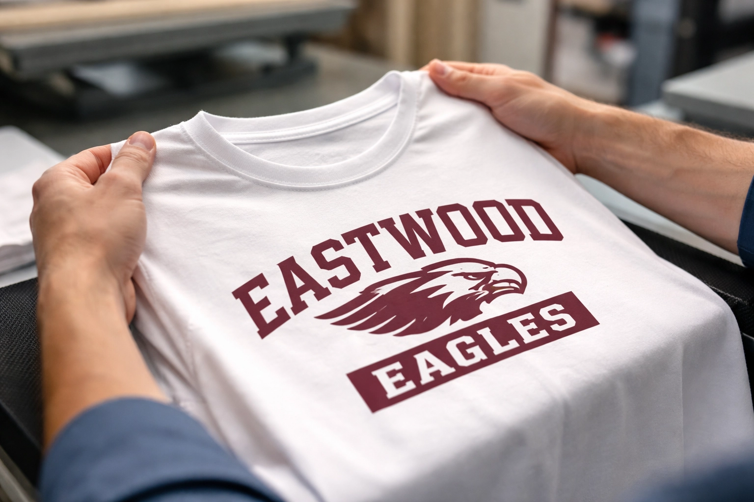Hands inspecting a maroon and white custom school shirt for print quality and reliability