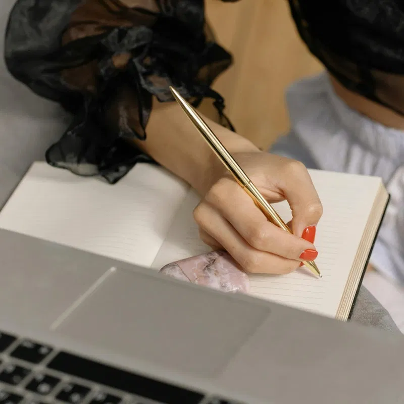 A person writing notes in a notebook next to a laptop, representing the focused planning phase of a content strategy.
