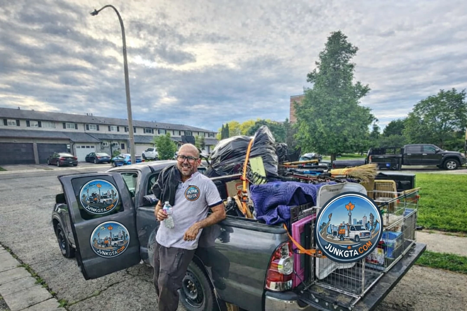 junk-removal-crew-full-load-residential.jpg A Junk GTA crew member stands beside a pickup truck loaded with various junk items, such as large bags, a broom, a pet cage, miscellaneous furniture, and household goods.