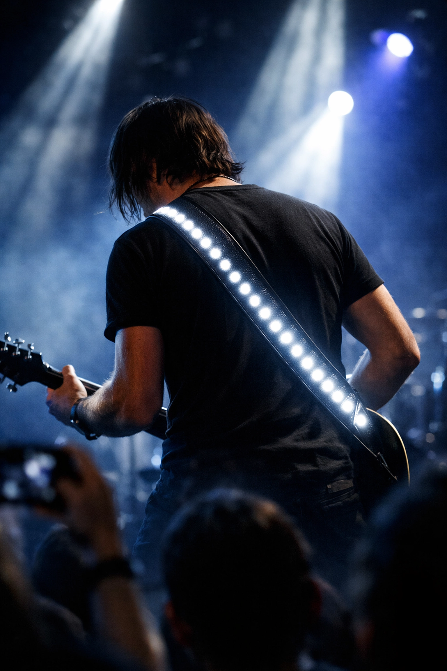 Guitarist performing on stage with glowing LED guitar strap in low lighting
