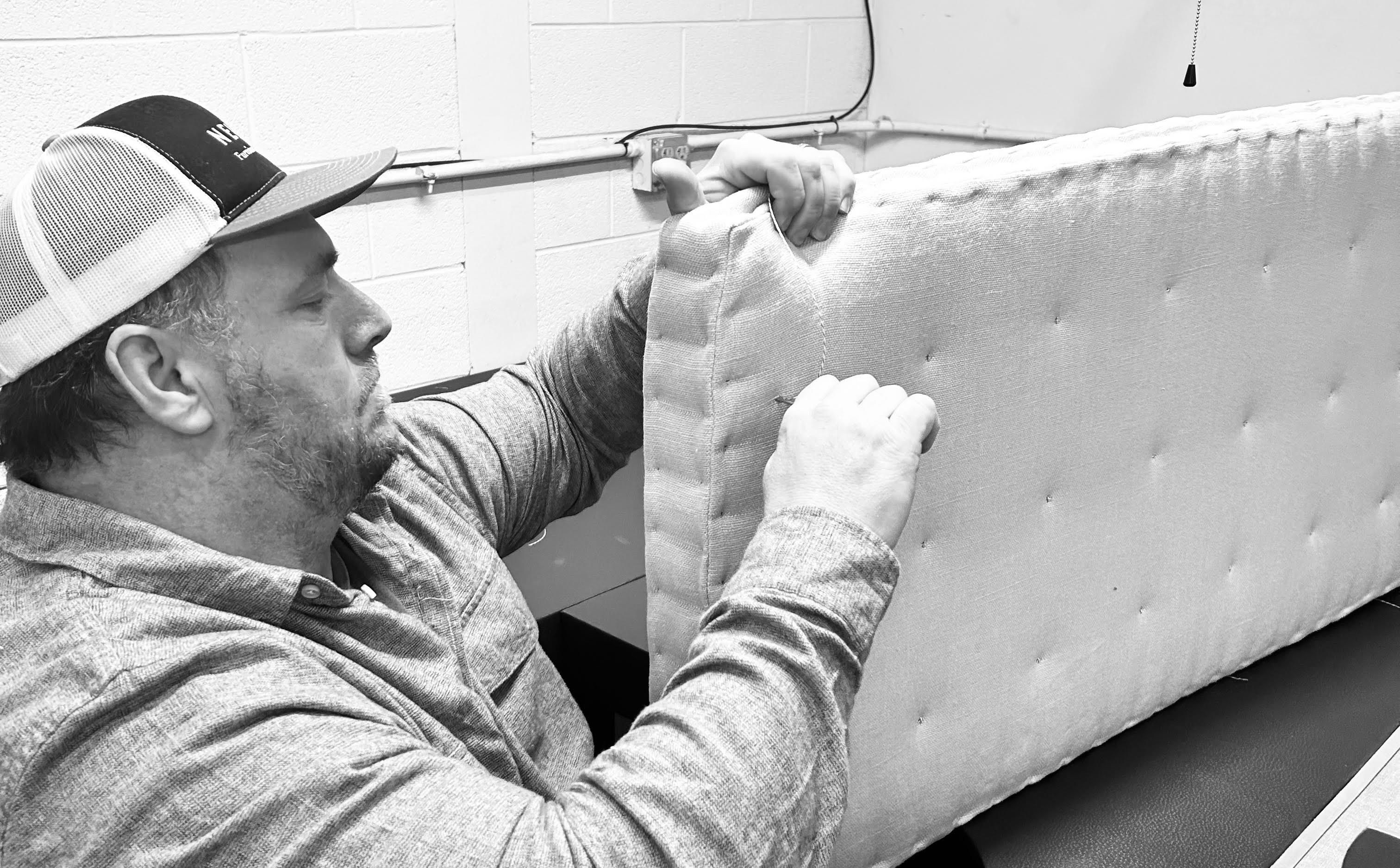 A skilled craftsman is hand-tufting stitches into the edge of a custom-upholstered cushion, ensuring precision and durability for a commercial furniture project.
