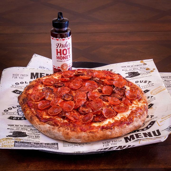 Triple Strike pizza with pepperoni, sausage, and ham on wooden peel