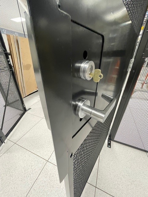 Close-up of a U.S. CAGE modular security door, featuring a heavy-duty lock and lever handle.