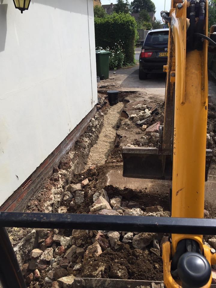 Excavator digging trench alongside a building