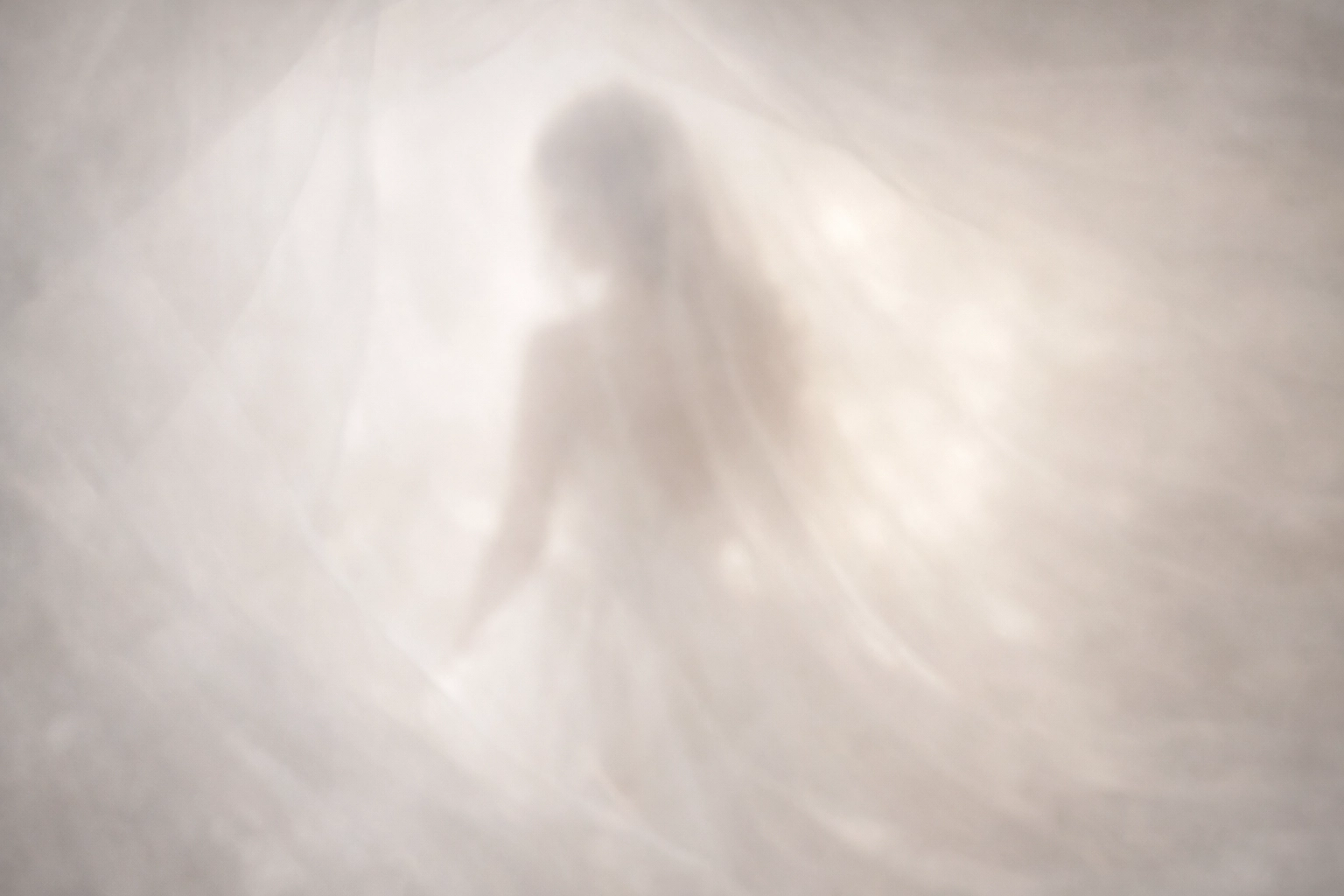 Ethereal bridal silhouette viewed through layers of romantic white tulle and soft gold light.