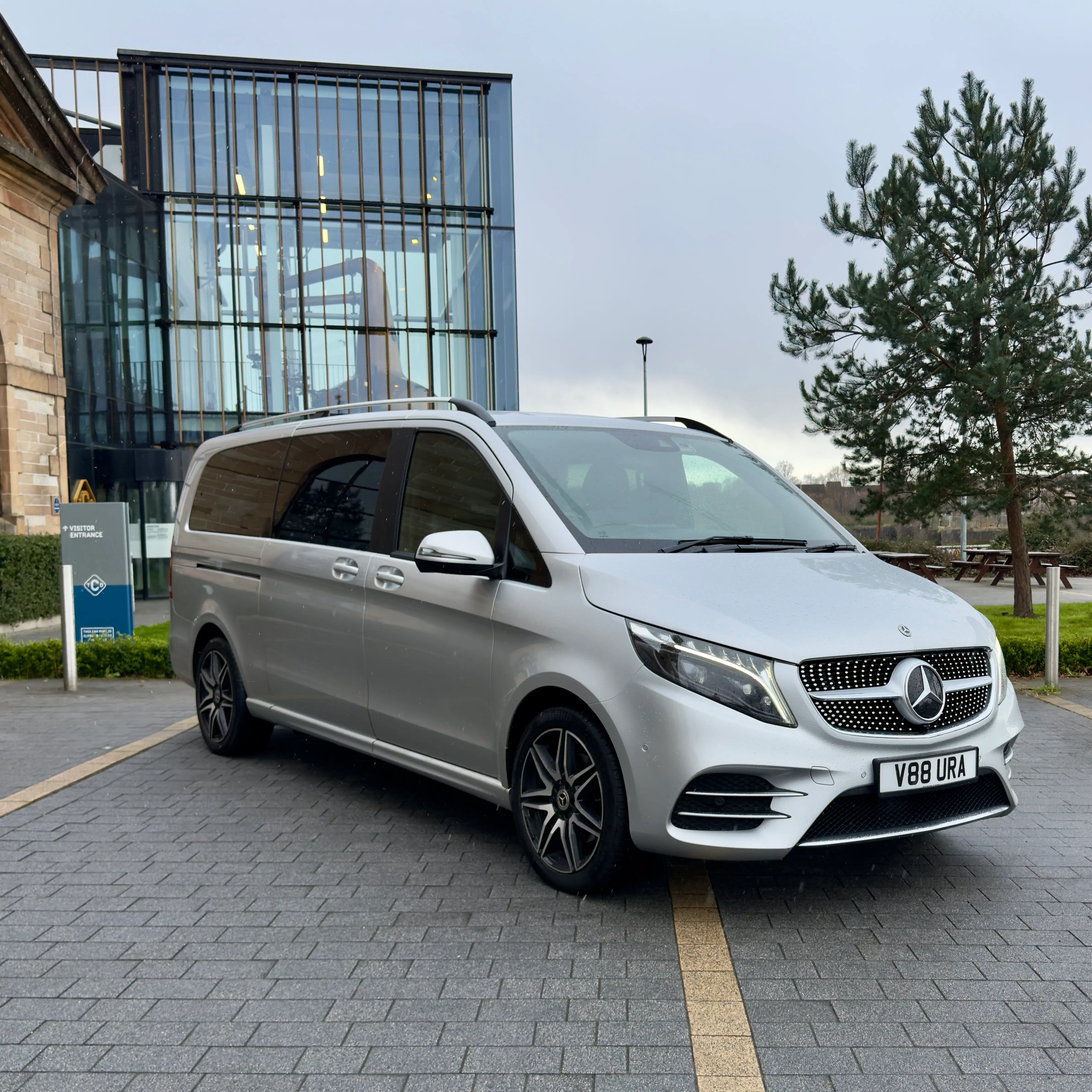 Premium silver Mercedes-Benz V-Class parked outside a modern glass building, ready for executive transfers